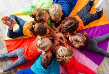 Eine Gruppe Kleinkinder liegt im Kreis und halten einander die Hände