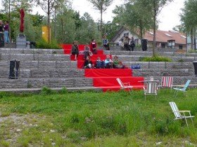 Rote Stoffbahn auf Steintreppe mit Menschengruppe sitzend.