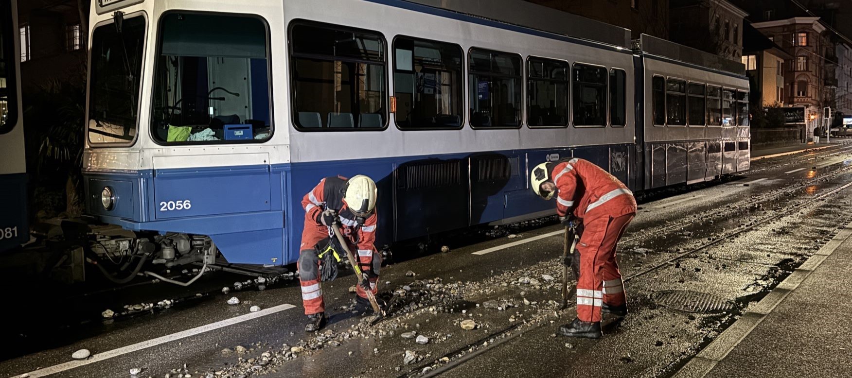 Nach einem Wasserrohrbruch befreien Feuerwehrleute die Gleise eines Trams von Steinen.
