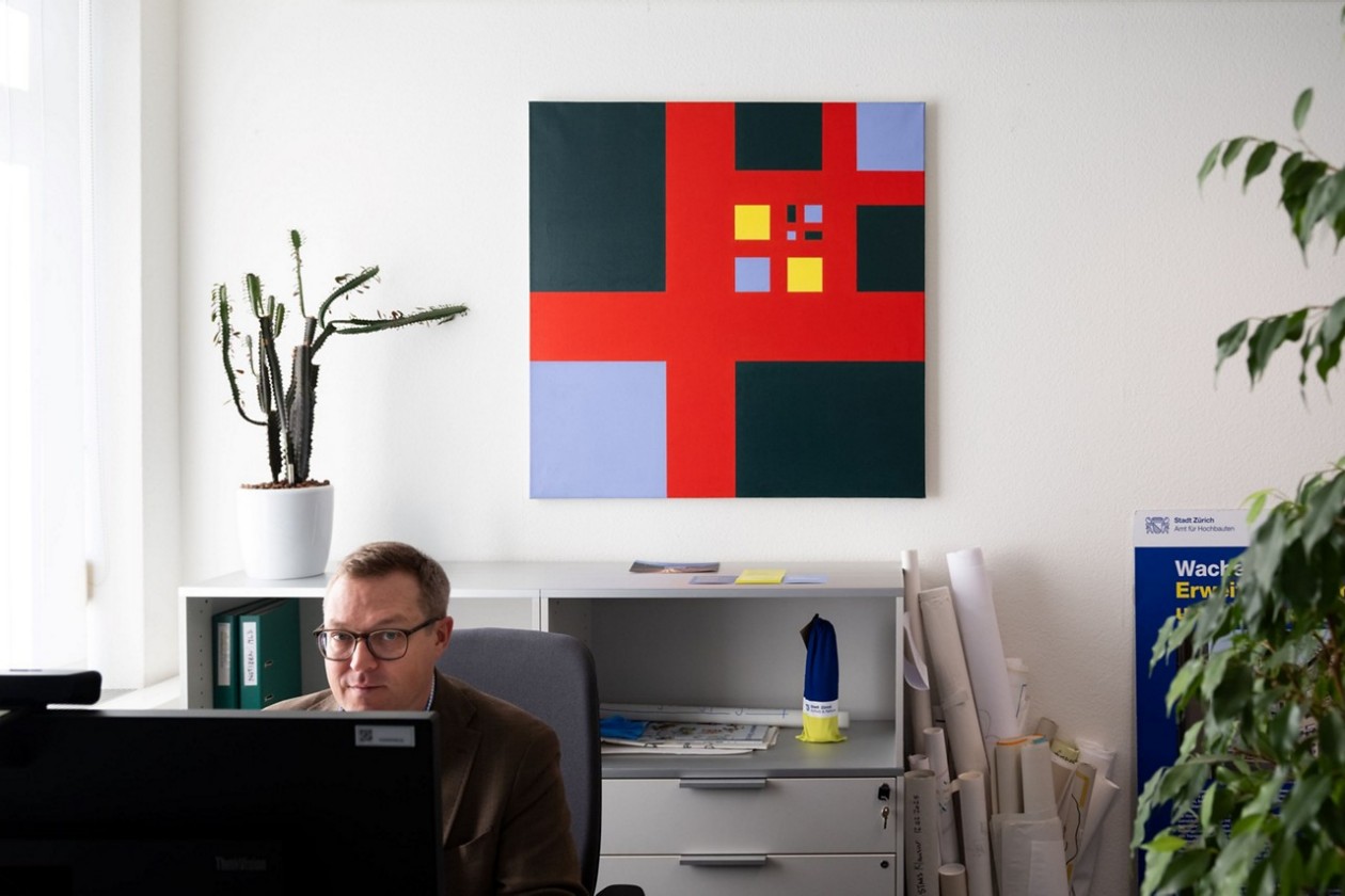 Daniel Müller sitzt in seinem Büro vor dem Kunstwerk «Vier Kreuzgruppen verbunden 1956/1966/3».