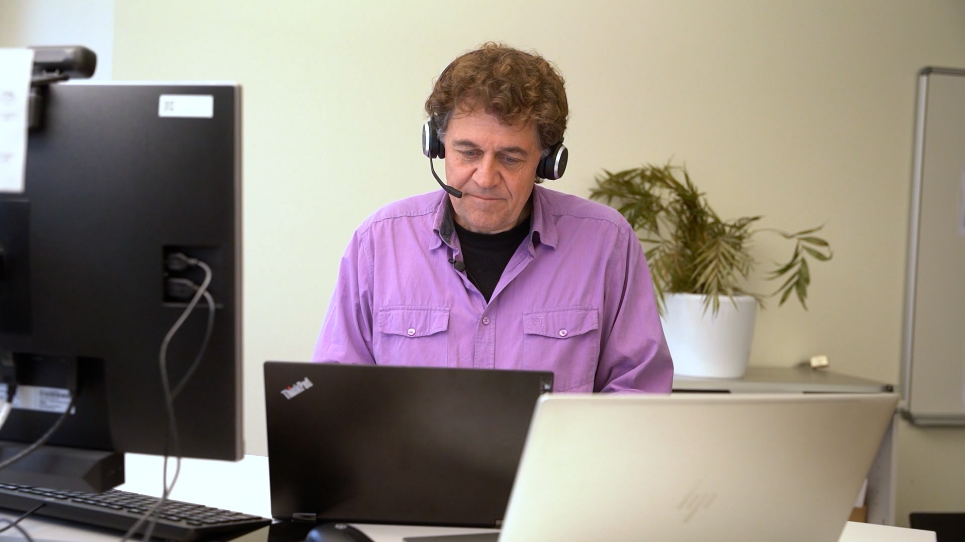 Bernhard Rüfenacht in violettem Hemd mit Headset am PC sitzend.
