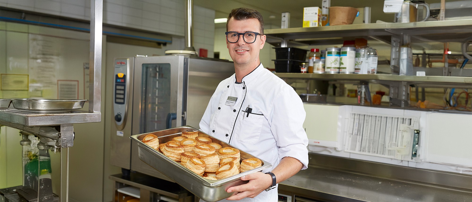 Stephan Wunderlich, Leiter Küche Gesundheitszentrum für das Alter, mit Blech in der Hand in weisser Arbeitskleidung.