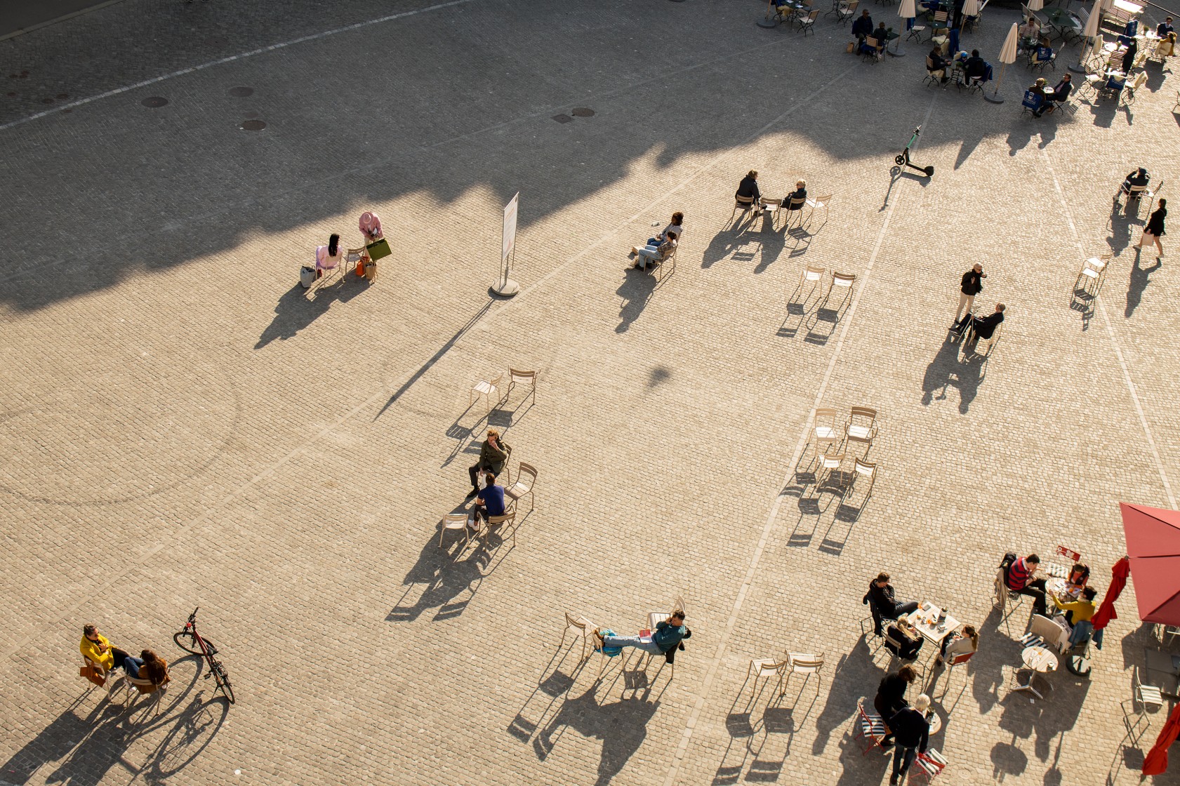 Luftaufnahme des Münsterhofs in Zürich: Eine lose Gruppe von Personen sitzt auf einzelnen Stühlen über den Platz verteilt.
