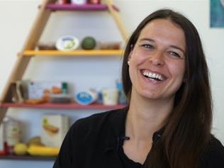 Luzia Müller ist rechts im Bild, sie lacht, im Hintergrund ist eine Ernährungspyramide zu sehen.