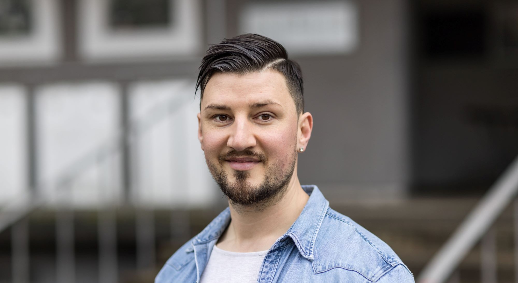 Ein Mann mit Jeanshemd und weissem T-Shirt steht draussen. Foto Alex Colle