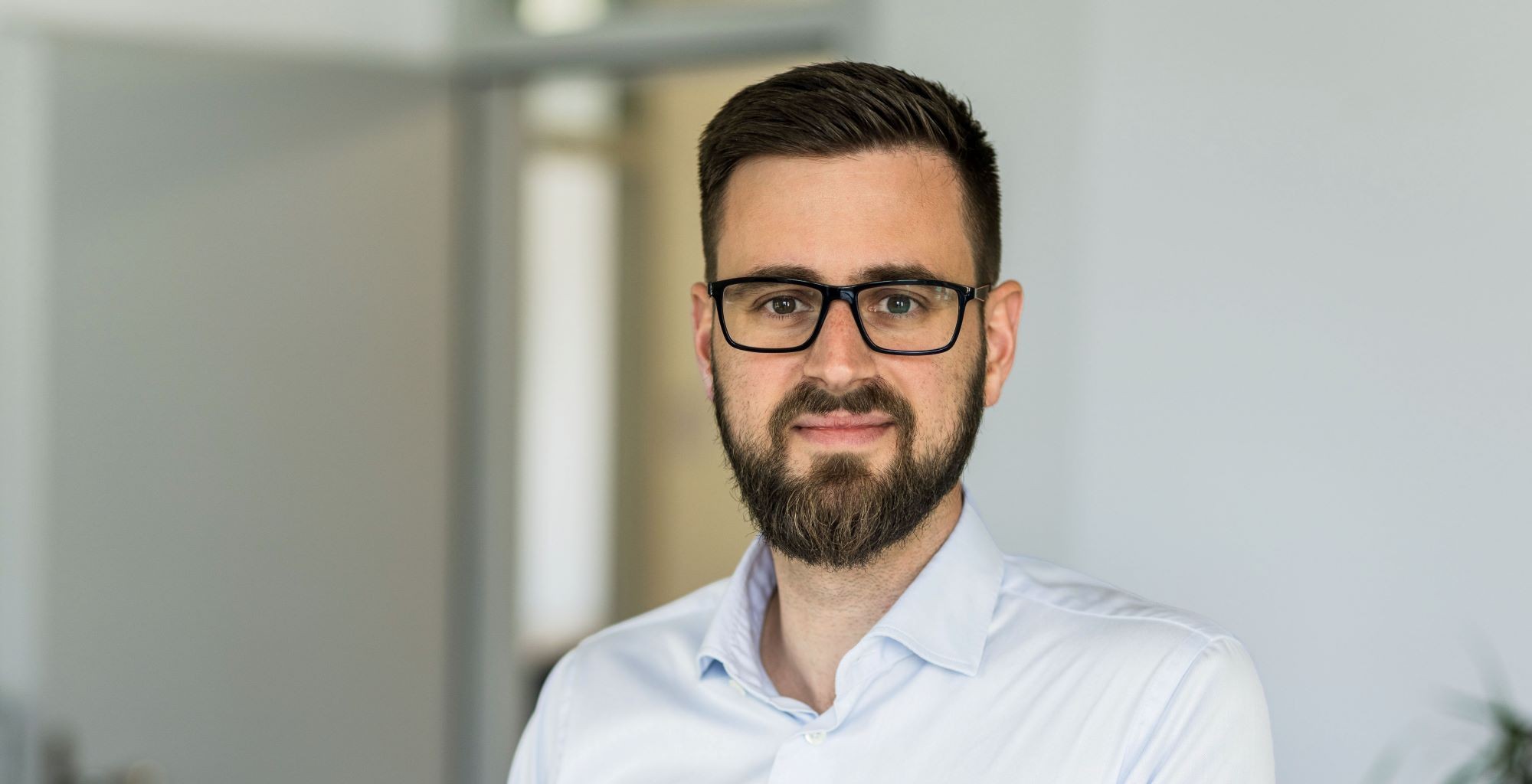 Man sieht einen lächelnden Mann mit kurzen Haaren, einem Bart, dunkler Kleidung. Foto Alex Colle