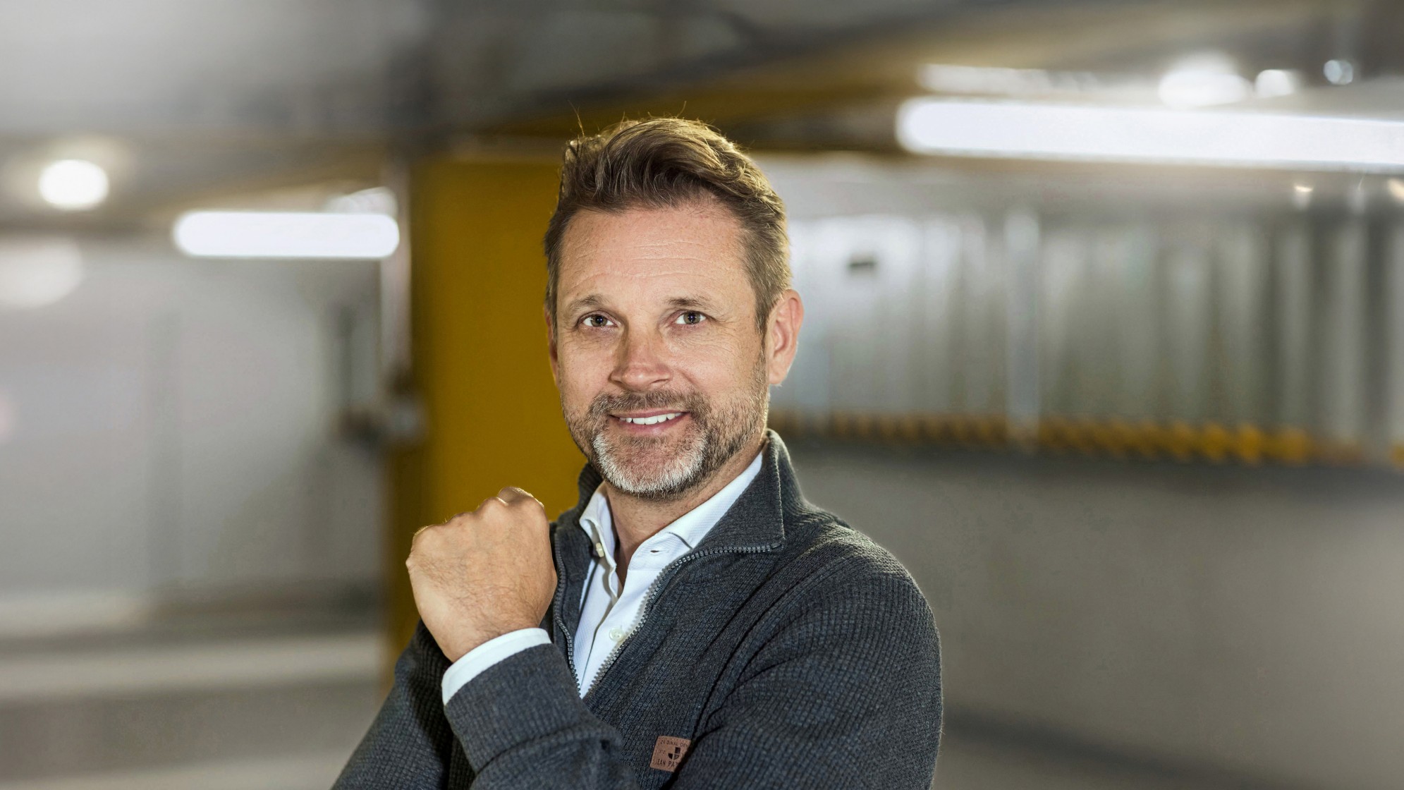 Man sieht einen lächelnden Mann mit kurzen Haaren, einem Bart, dunkler Kleidung. Foto Alex Colle