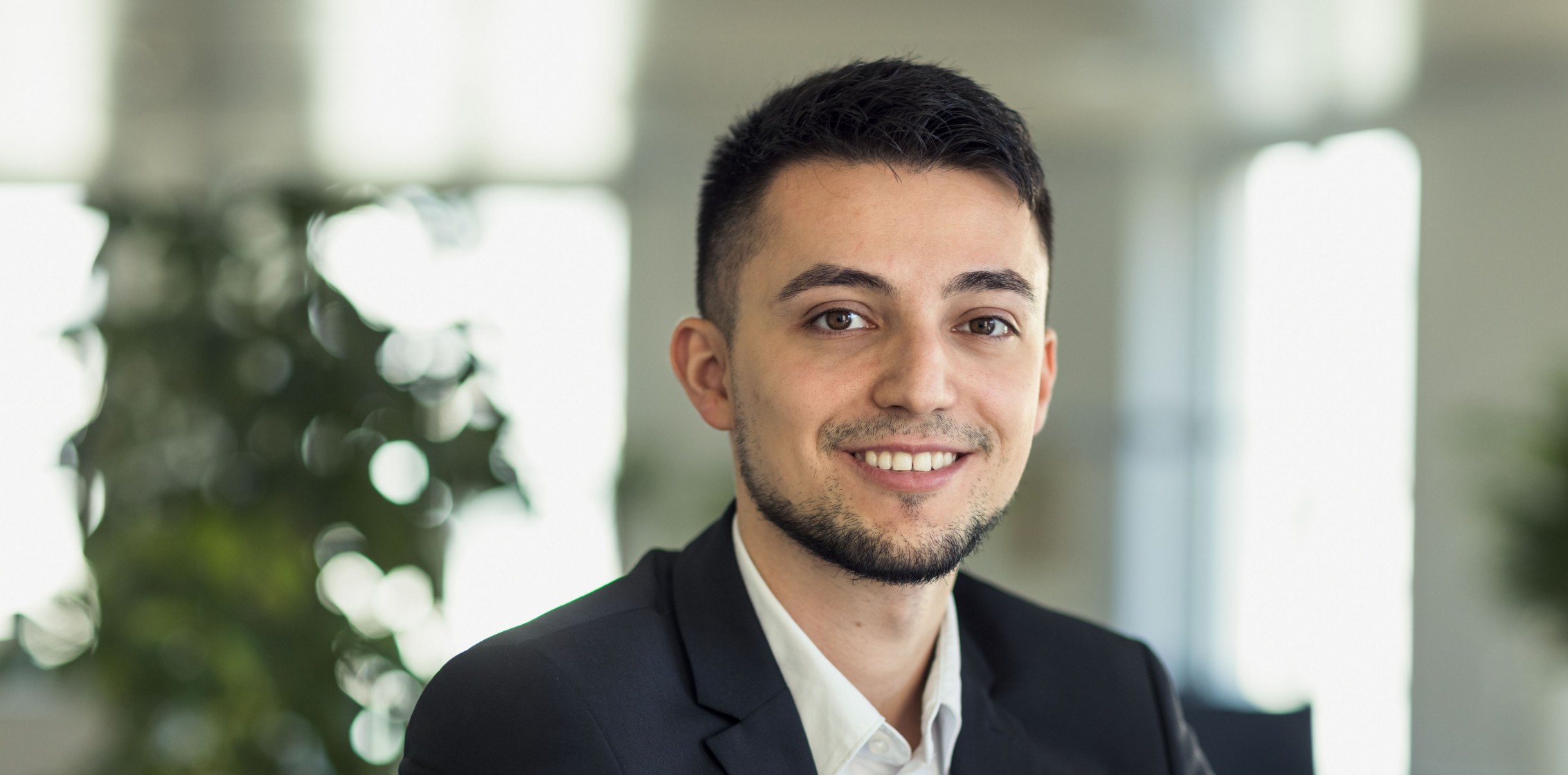 Ein lächelnder Mann mit dunklen Haaren und Anzug. Foto Alex Colle