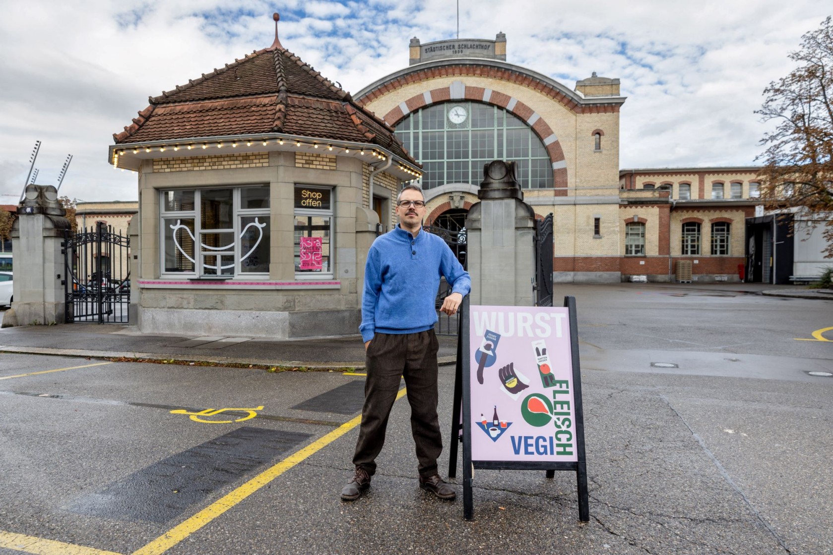 Ein Mann mit blauer Jacke steckt neben einem aufgestellten Schild. Im Hintergrund ist das Schlachthof-Areal zu sehen. Foto Alex Colle