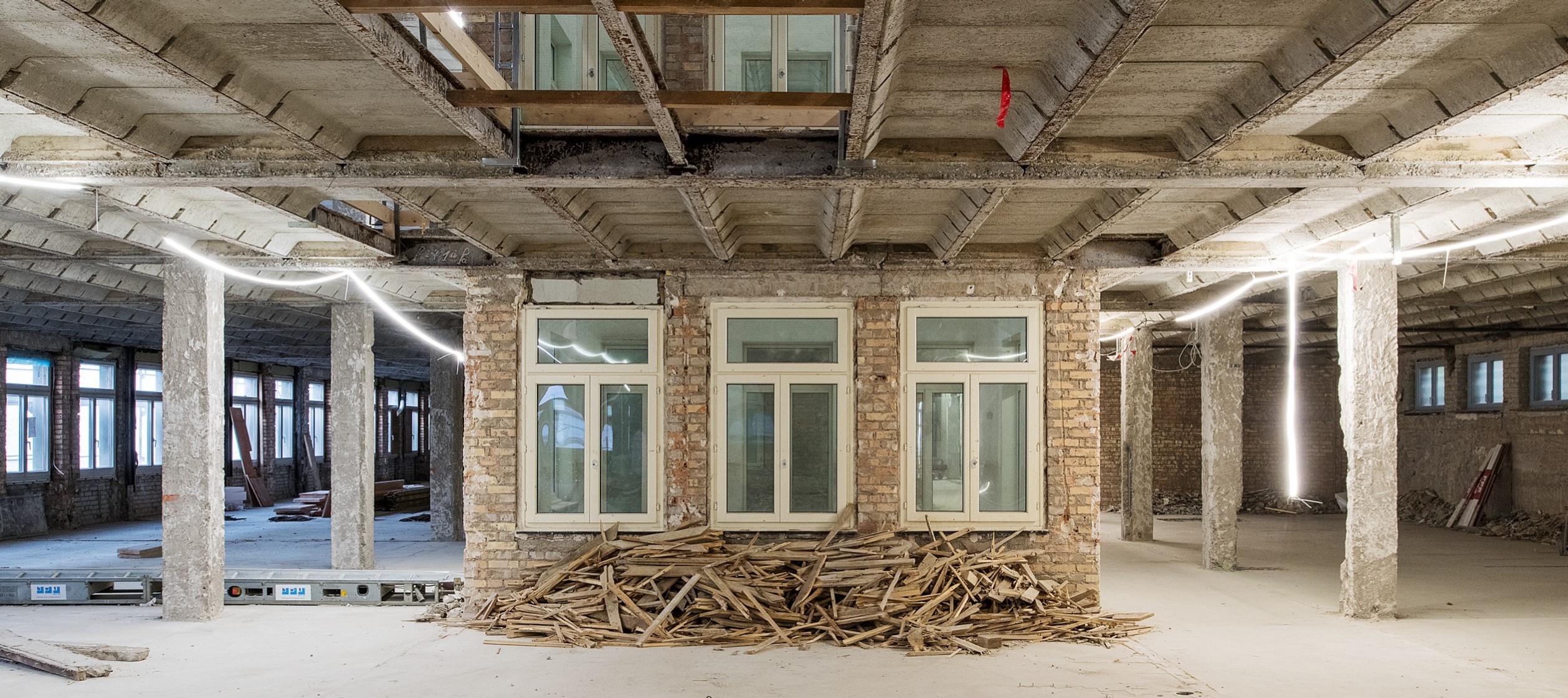 Ausgehöhltes Innere eines Gebäudes, sichtbare Tragstützen und drei Fenster zu einem Innenhof