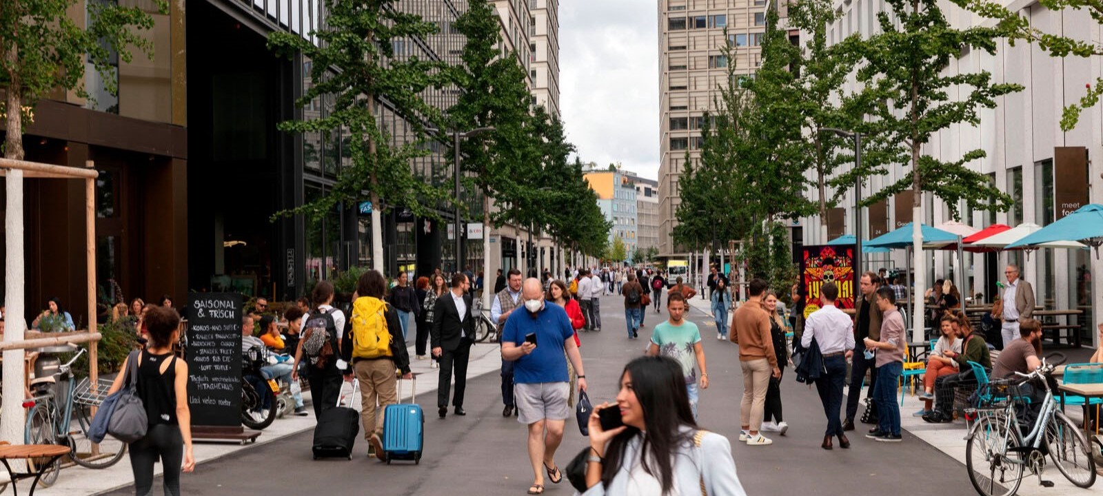 Die Europaallee in Zürich: Zwischen zwei Häuserzeilen laufen viele Menschen vorbei, bunte Sonnenschirme stehen vor einem Café.