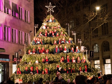 11-Christmas-Tree In der Altstadt ist ein Gerüst aufgebaut und als Weihnachtsbaum dekoriert worden. Darauf stehen Kinder als Samichläuse verkleidet uns singen.