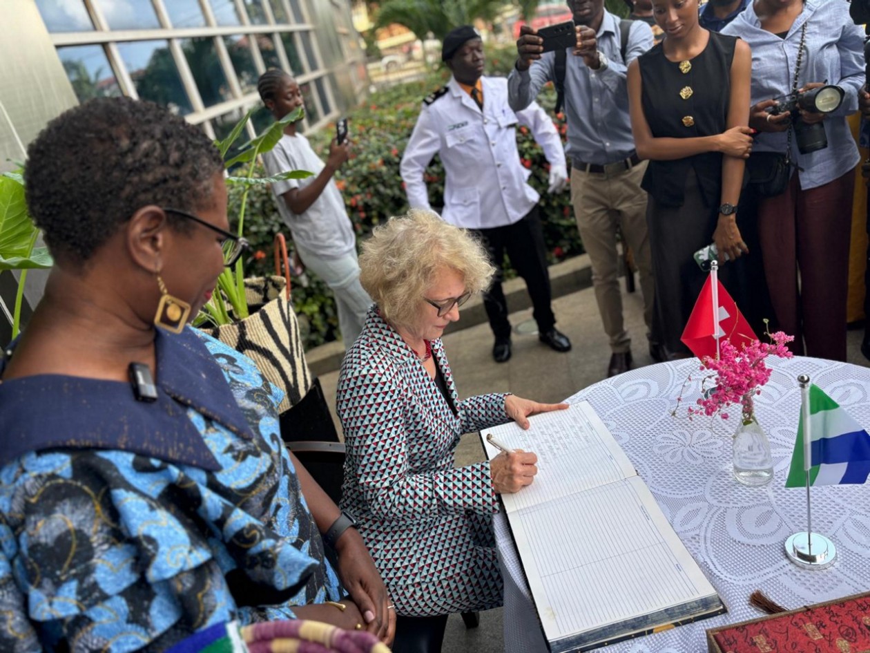 Stadtpräsidentin Corine Mauch setzt ihre Unterschrift in ein Buch, umringt von Würdenträger*innen von Freetown.