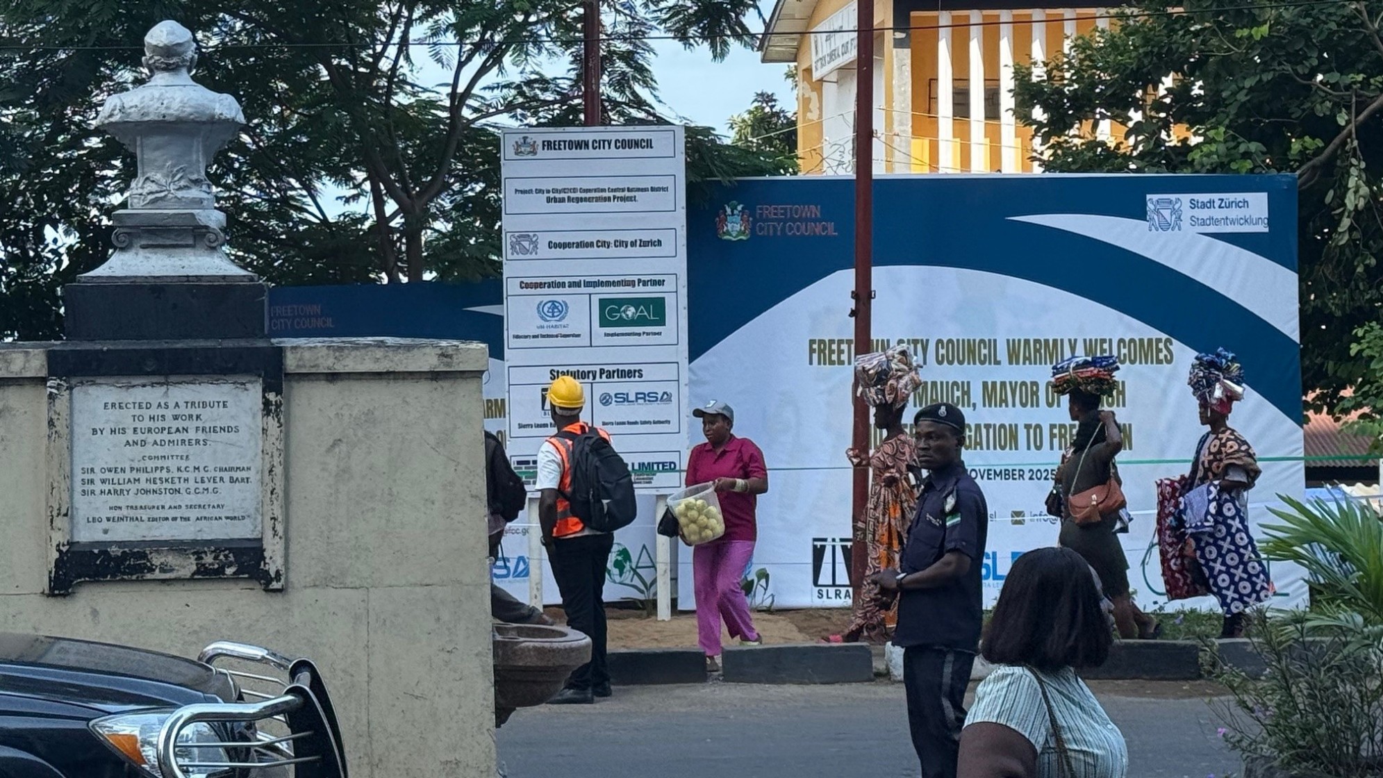 Die Zürcher Stadtpräsidentin und die Bürgermeisterin von Freetown laufen durch eine Strasse von Freetown, sekundiert von Bodyguards.
