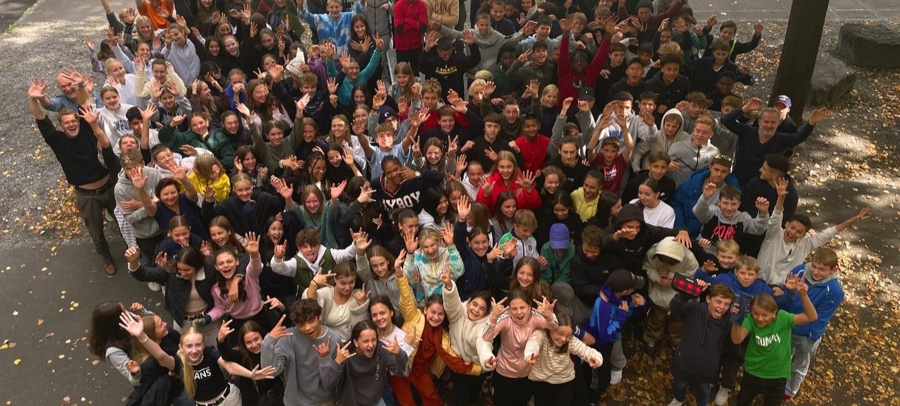 Blick von obern auf eine grosse Gruppe von Schüler*innen und Lehrer*innen, die dem*r Fotograf*in zuwinken.
