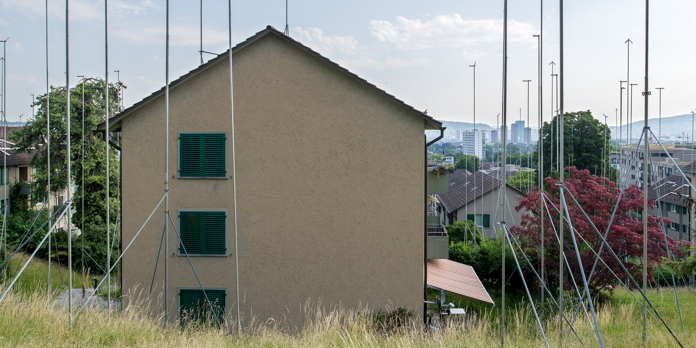 Um einen alten Wohnblock  stehen hohe Stangen, die anzeigen, wie hoch der Ersatzneubau werden soll. 