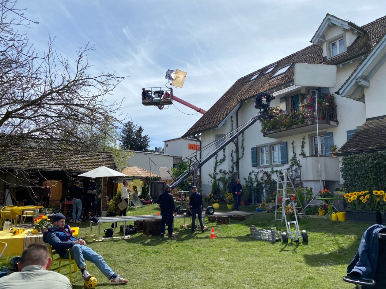 Auf dem Bild ein Mehrfamilienhaus, um das die Crew Krane, Scheinwerfer und Blitzschirme aufgebaut hat.