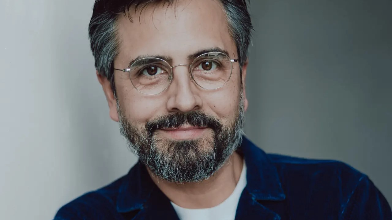 Rafael Sanchez blickt mit Zuversicht in die Kamera.  Er hat einen kurzen Bart, die Haare leicht angegraut und trägt eine Brille mit dünnem Goldrand.