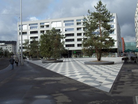 Im Vordergrund der Max-Bill-Platz mit seinem markanten geometrischen Muster. Dahinter eine moderne Liegenschaft.