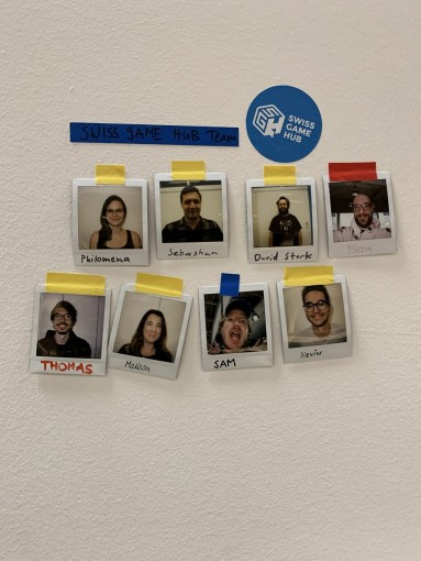 Poträtfotos des Teams hängen an einer Wand, behelfsmässig mit farbigen Klebestreifen angehängt.