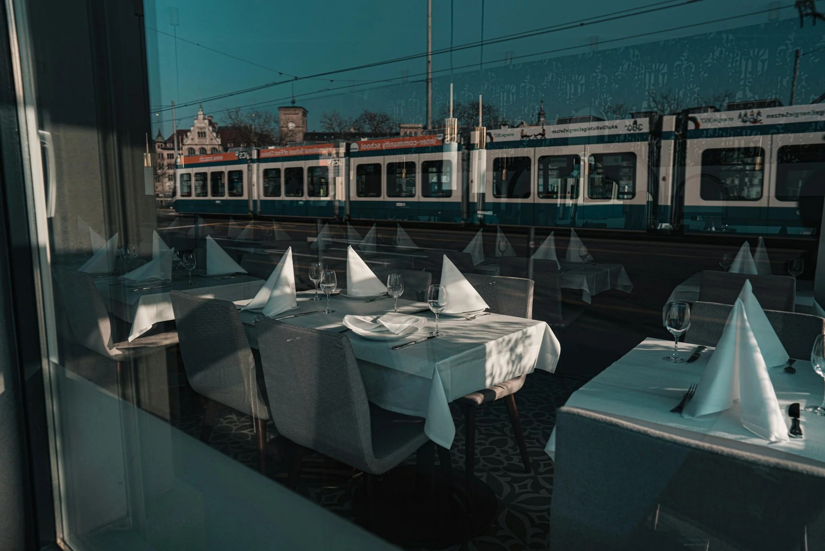 Hinter dem grossen Fenster sieht man weiss gedeckte Tische, im Fenster spiegelt sich ein vorbeifahrendes Tram.