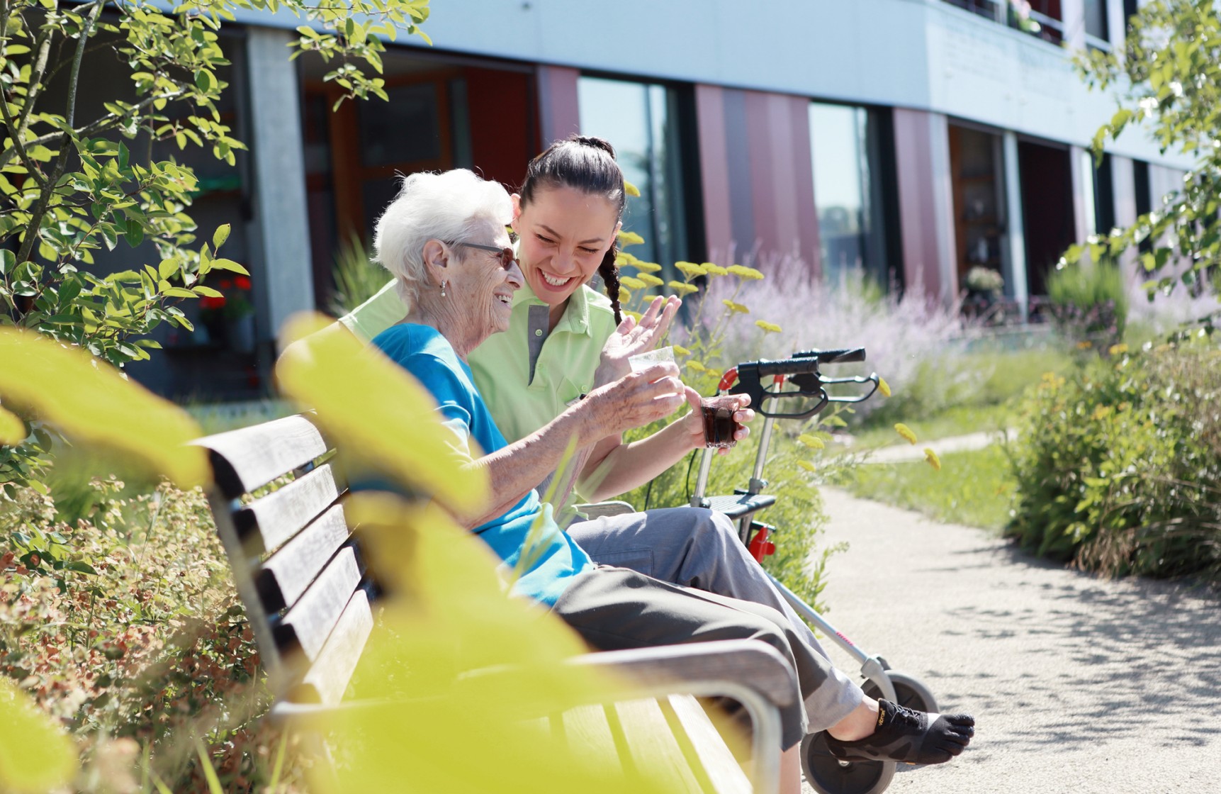 Eine Mitarbeitende der Pflege sitz mit einer Bewohnenden im Garten auf einer Bank.