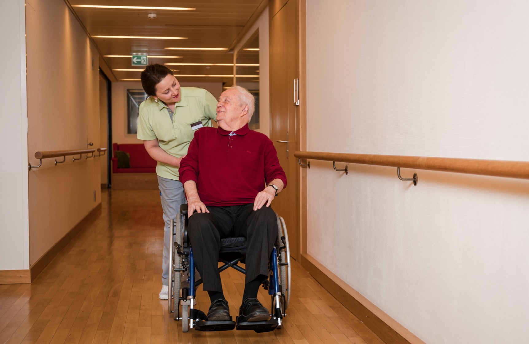 Mitarbeitende der Pflege begleitet einen Bewohnenden im Rollstuhl.