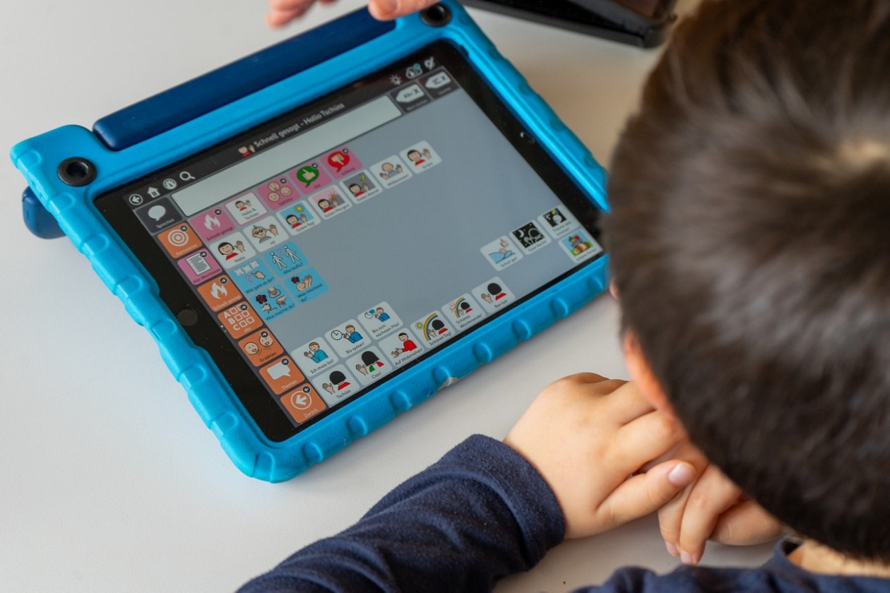 ein kleiner Junge schaut auf ein Tablet mit Piktogramme
