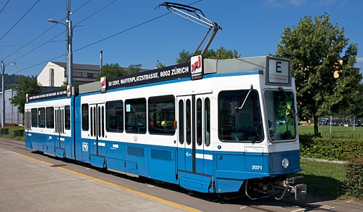 Eine blau-weiße Tram 2000 steht auf einer Straße in einer städtischen Umgebung.