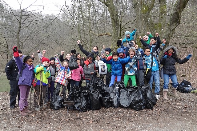 Das Bild zeigt jubelnde Kinder im Wald mit den gesammelten Müllsäcken.
