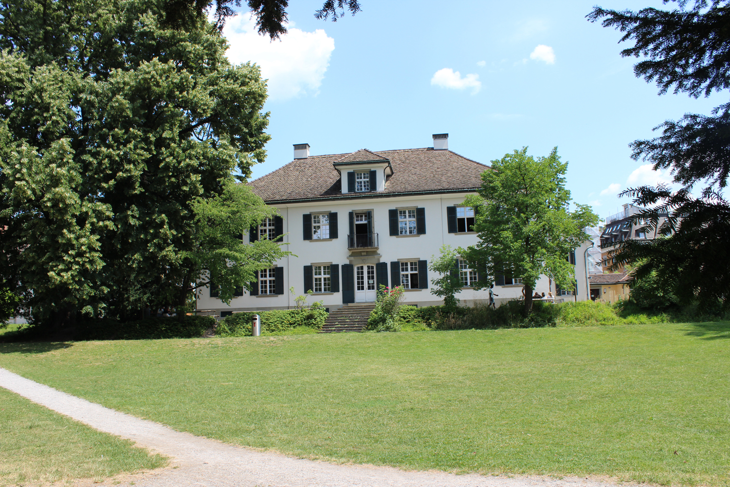 Das Bild zeigt das Herrenhaus Beckenhof mit einer grünen Wiese und grossen Bäumen. 