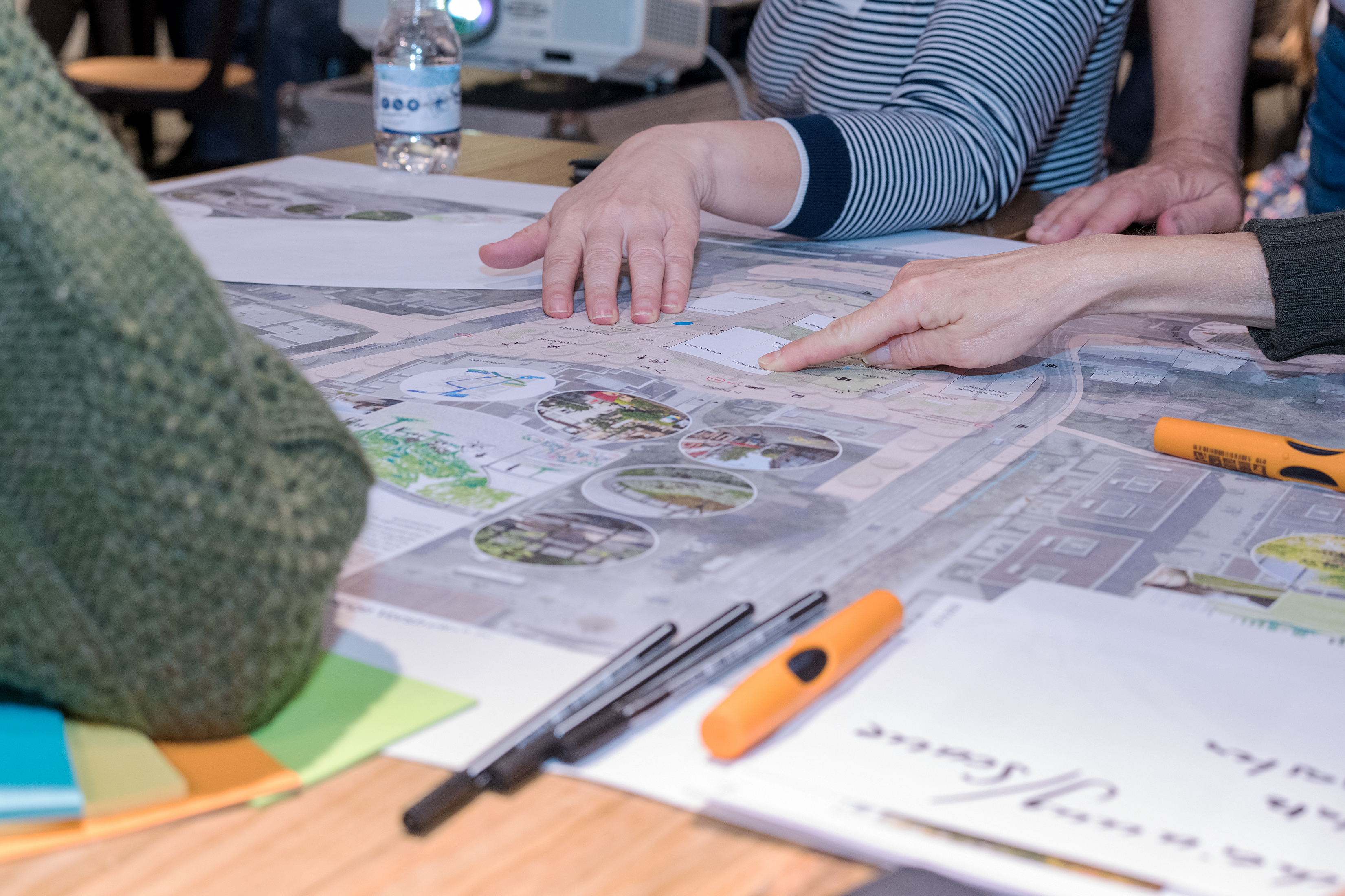 Personen sitzen in einem Workshop im Zentrum Affoltern in Zürich um einen Tisch. Auf dem Tisch liegen Unterlagen und Materialien für Gruppenarbeiten..