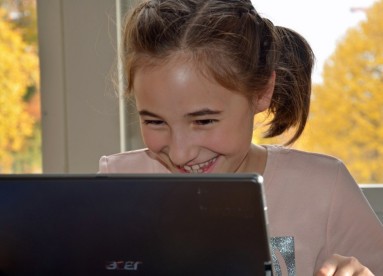 Foto von einem lachenden Kind, das in einen Laptop blickt.
