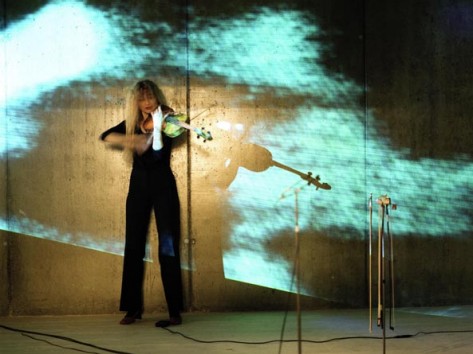 Frau spielt Geige vor Betonwand mit Bildprojektion