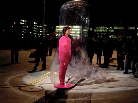 Rosa gekleidete Frau steht in transparentem aufgeblasenen Fuss, welcher mit rosa Flüssigkeit gefüllt wird