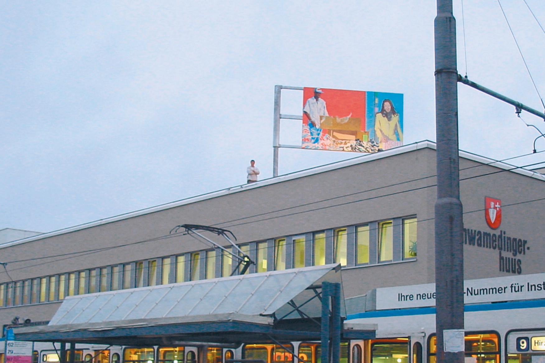 Tramstation, dahinter Gebäude mit farbig bemaltem Bild auf dem Dach