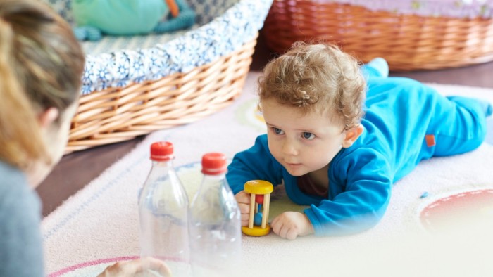 Eine Fachfrau Betreuung zeigt dem krabbelndenn Kleinkind ein Spiel mit zwei leeren PET-Flaschen