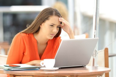 Eine Frau sitzt mit besorgtem Gesichtausdruck vor einem Laptop und schaut auf den Bildschirm