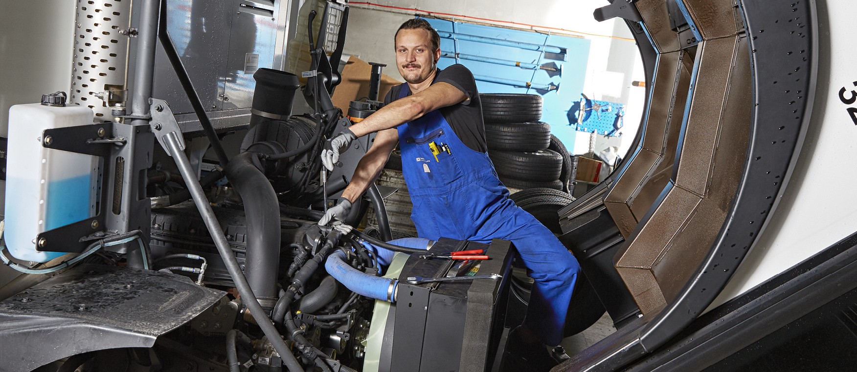 Ein/e lernende/r Automobil-Fachfrau/-mann EFZ Nutzfahrzeuge oder Personenwagen mit einer blauen Latzhose repariert die Führerkabine eines Lastwagens.
