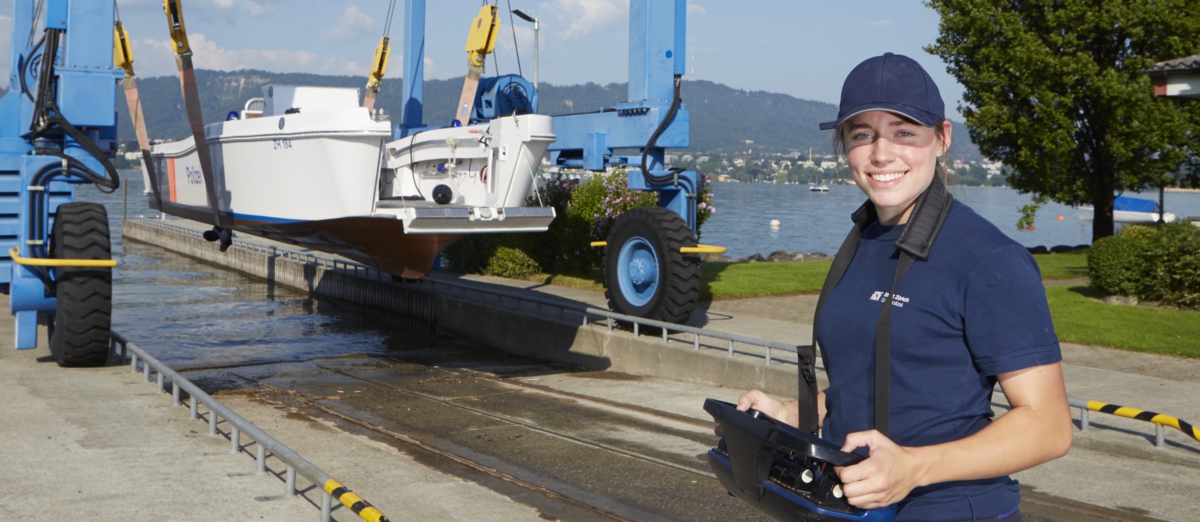 Ein/e lernende/r Bootfachwart/in EFZ in blauem Poloshirt und Schirmmütze wässert ein Boot mit Fernsteuerung in den Zürichsee ein.