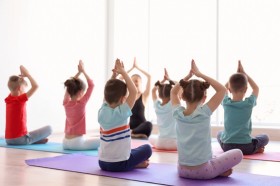 Eine Kindergruppe die auf Yogamatten sitzt und die Hände in die Luft streckt