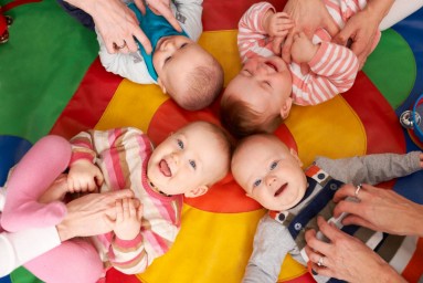 Bild mit sechs Elternteilen, die am Boden liegen und ihre Babys nach oben heben. Babys sind in Windeln. 