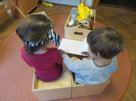 Zwei Kinder sitzen zusammen vor ihnen Masken und ein Block Papier.