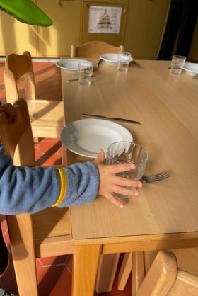 Eine Hand greift nach Glas auf einem kleinen Kindertisch. Im HIntergrund sieht man noch mehr Teller und Gläser, die getischt wurden. 