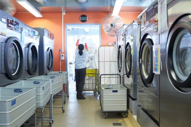 Ein Frau hebt einen Sack Wäsche in einem Raum mit mehreren Waschmaschinen.