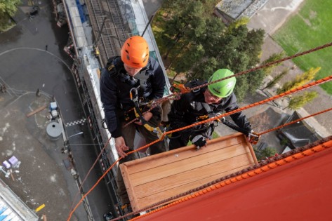 Das Bild zeigt zwei Personen, die am Kletterseil hängend, ein Falkenbrett am Kamin der ehemaligen Kehrrichtverwertungsanlage in Zürich anbringen.