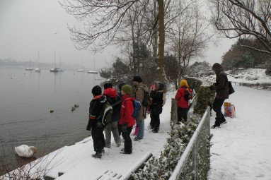 Kinder stehen am schneebedeckten Seeufer.