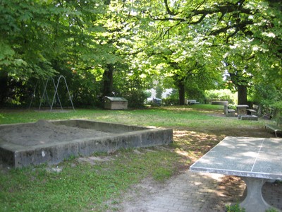 Möhrli-/Schanzackerstrasse. Kleinpark mit Spielgeräten und Feuerstelle, durch Bäume, Hecken und Mauern begrenzt.