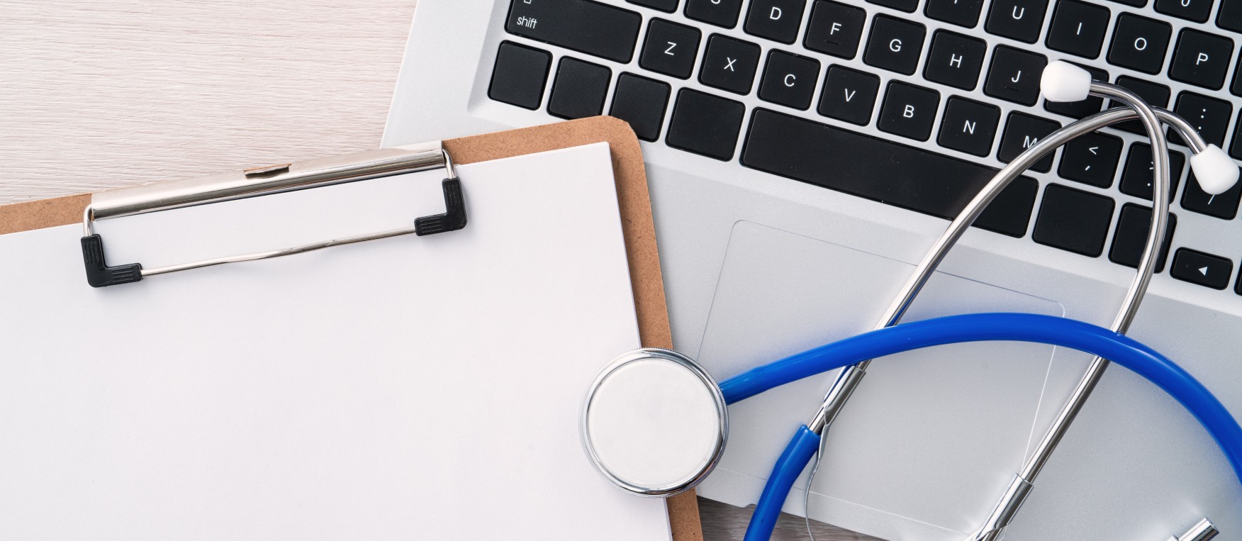 Stethoscope on laptop computer keyboard with medical record clipboard design concept.