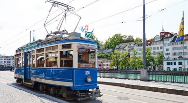 The blue VBZ Gourmet Line Tram driving along the rails next to the Limmat river.